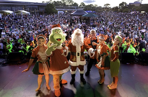 Santa and Christmas helpers stand on stage with a giant crowd behind them