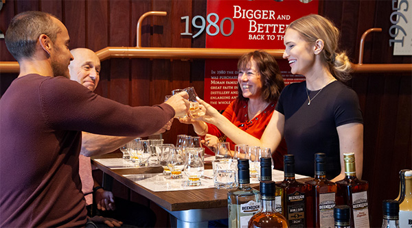 small group of men and women stand around table smiling and drinking craft beer