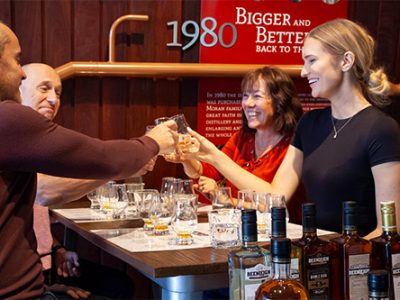 small group of men and women stand around table smiling and drinking craft beer