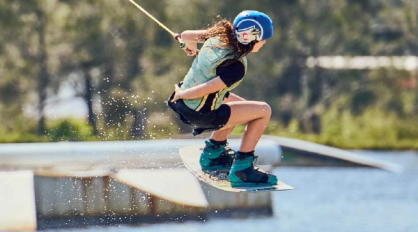 Girl wearing helmet and life vest holds onto a rope and wakeboards